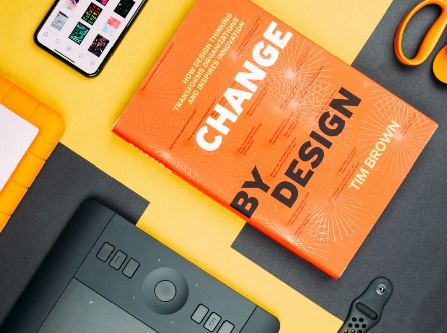 "Change by design" book on UX Design on a yellow background with some gadgets around it like Apple Watch iPhone