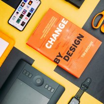 "Change by design" book on UX Design on a yellow background with some gadgets around it like Apple Watch iPhone
